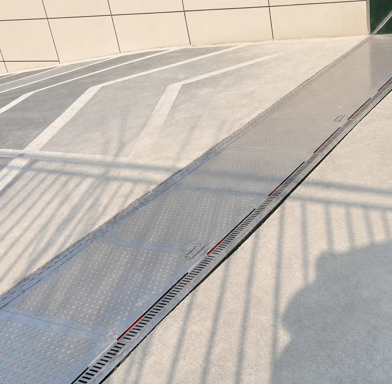 Passive flood barrier lying flush across a paved roadway, its patterned steel top plate level with the surface