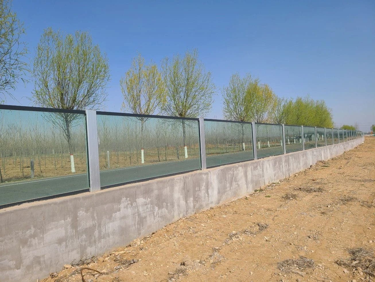 Glass flood wall with aluminum posts along an embankment road